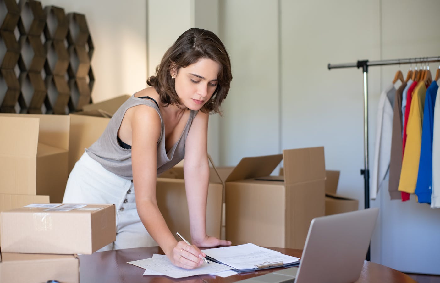 Small business owner reviewing notes beside a laptop and shipping boxes.